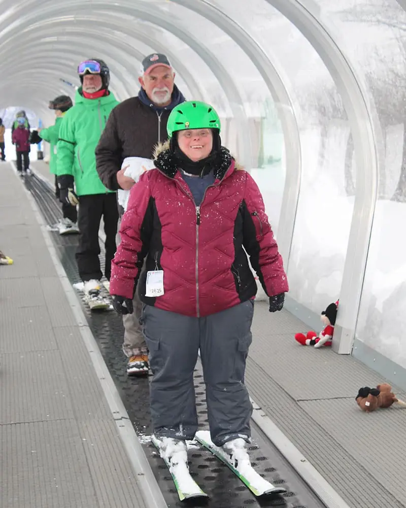 A participant in a ski helmet riding the covered conveyor lift at a ski area