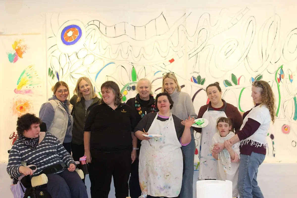 Participants and artists gathered in front of a large mural in progress