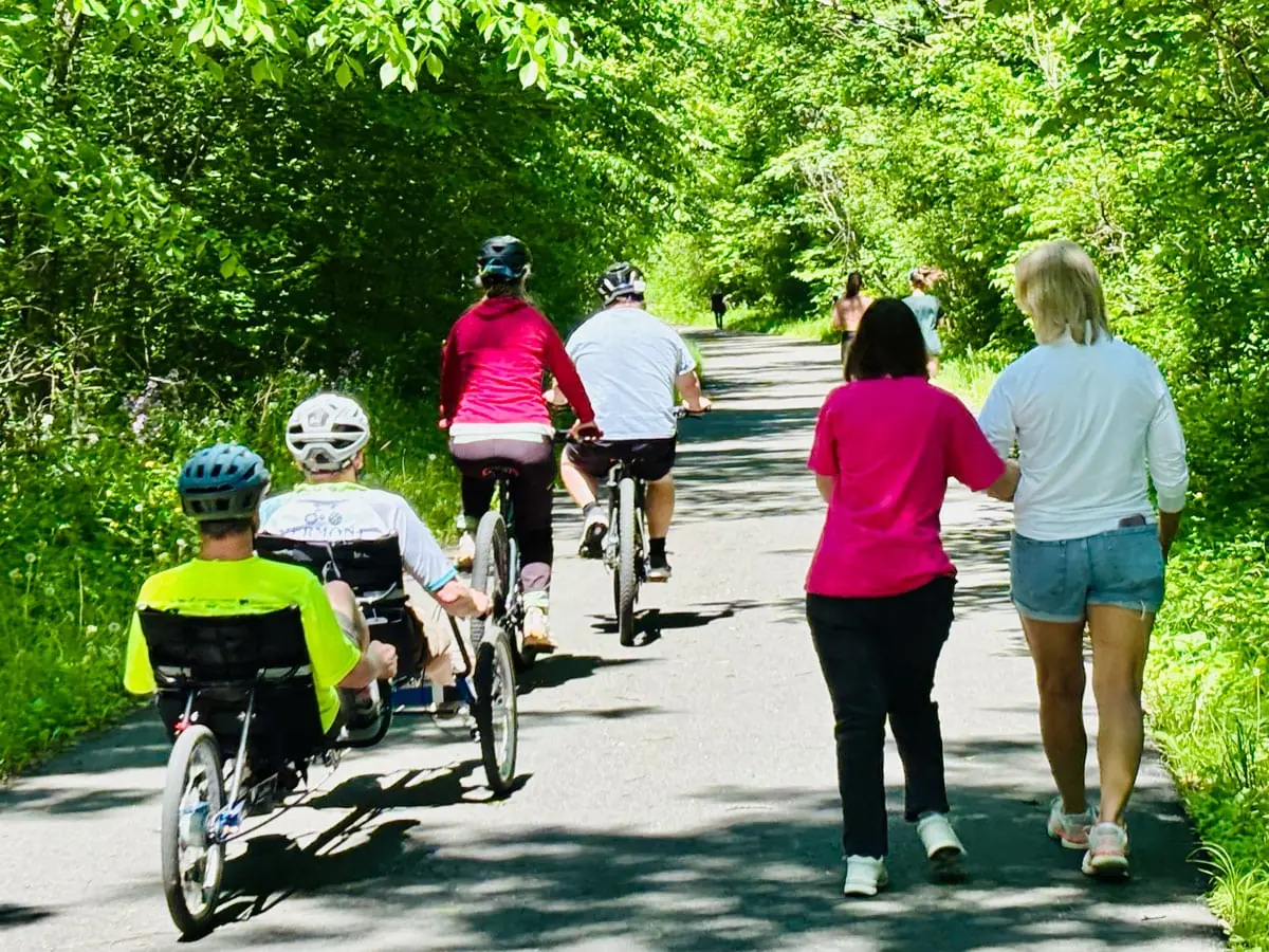 Volunteers walking and riding bikes with participants on a shaded path